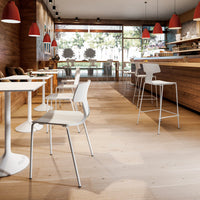 Modern white chairs with circular and square tables, set against warm wood and red pendant lights in a cozy café interior.