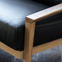 Black leather seat with natural wood frame, showcasing a modern minimalist design and sleek lines.