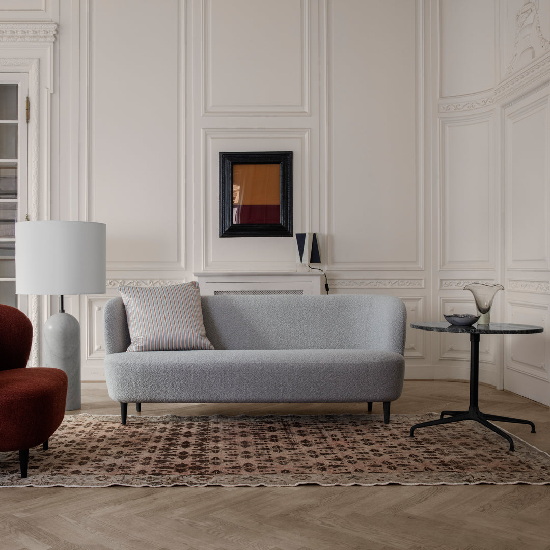 Gray modern sofa with light gray cushions, red accent chair, black glass table, and geometric area rug.
