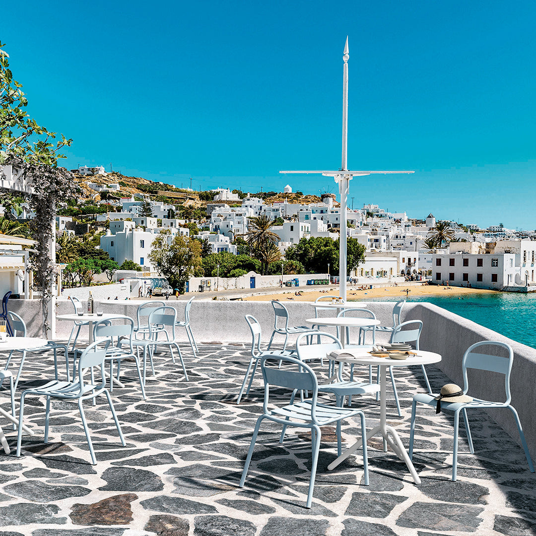 White chairs against a stone patio, featuring a vibrant blue sky and turquoise water backdrop.