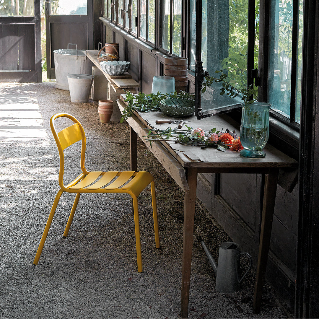 Bright yellow striped chair beside a rustic wooden table, accented with greenery and colorful decor in a sunlit setting.