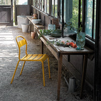 Bright yellow striped chair beside a rustic wooden table, accented with greenery and colorful decor in a sunlit setting.