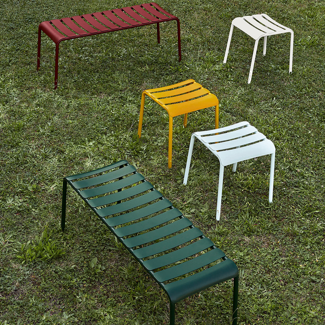 Assorted metal stools in red, yellow, green, white, and dark green with slatted patterns on a grassy background.