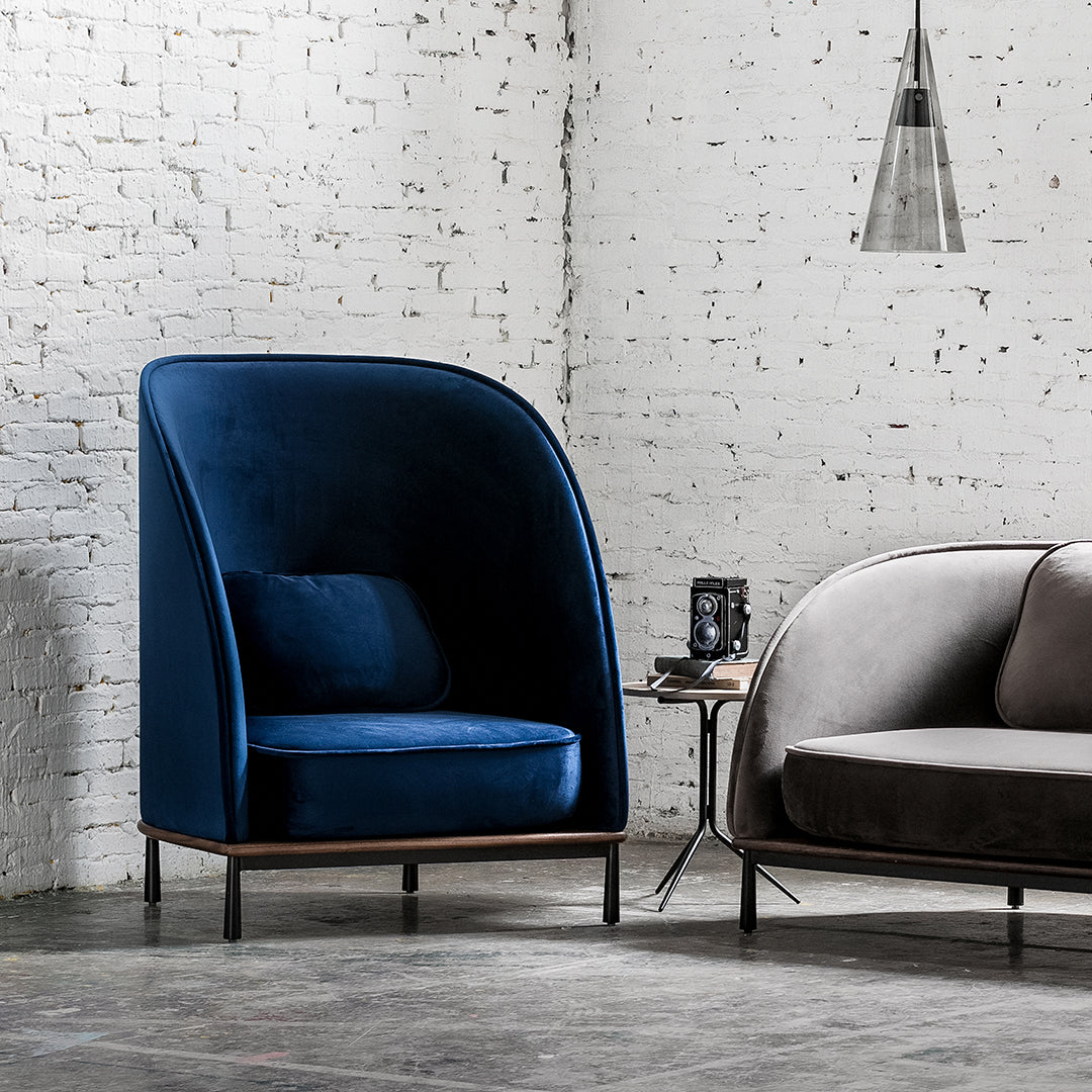 "Deep blue velvet armchair with smooth, curved lines against a textured white brick wall."