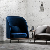 "Deep blue velvet armchair with smooth, curved lines against a textured white brick wall."