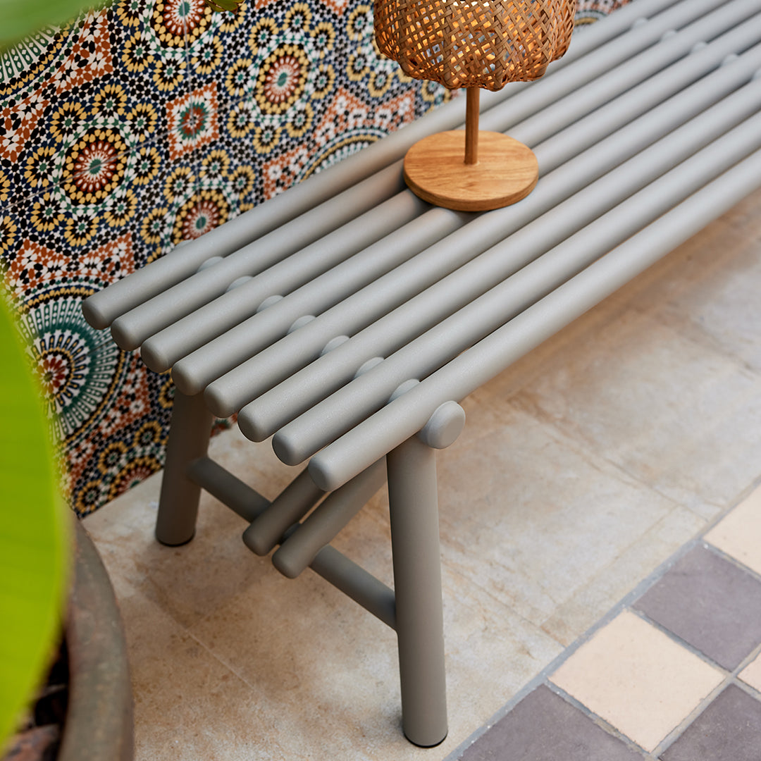 Gray slatted bench with a geometric patterned backdrop, featuring vibrant colors and bohemian style.