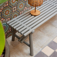 Gray slatted bench with a geometric patterned backdrop, featuring vibrant colors and bohemian style.