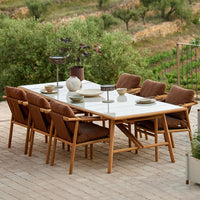 Dining table with a white marble top and beige upholstered chairs, featuring natural wood accents and a textured outdoor setting.
