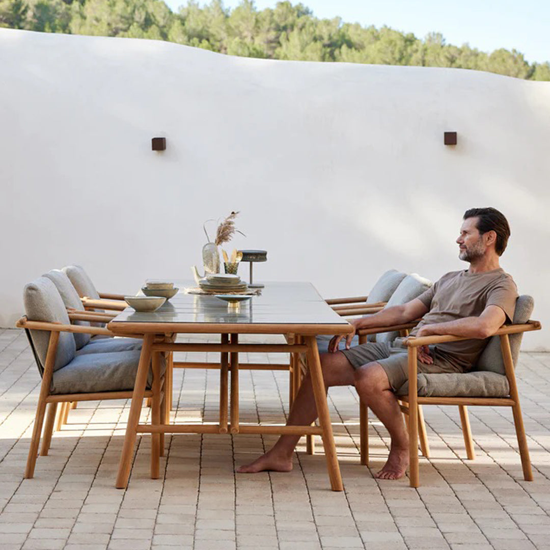 Light gray cushions on wooden chairs around a sleek, stone-colored table, set against a neutral backdrop.