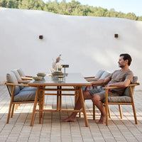 Light gray cushions on wooden chairs around a sleek, stone-colored table, set against a neutral backdrop.