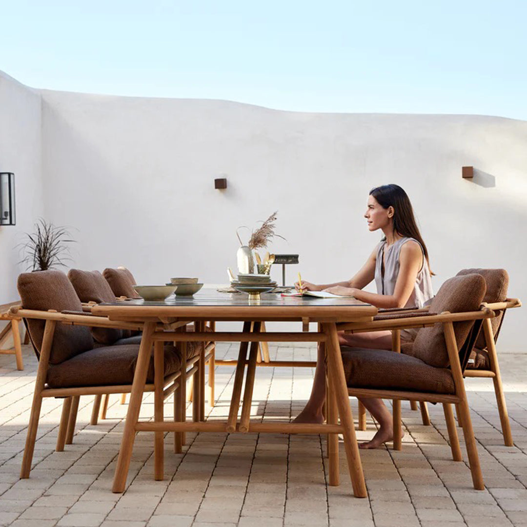 Modern patio dining set featuring brown upholstered chairs and a natural wood table against a minimalist white background.