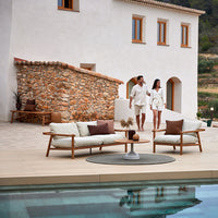 "Natural stone wall, soft beige cushions, and rich brown accent pillows blend harmoniously in an outdoor setting."