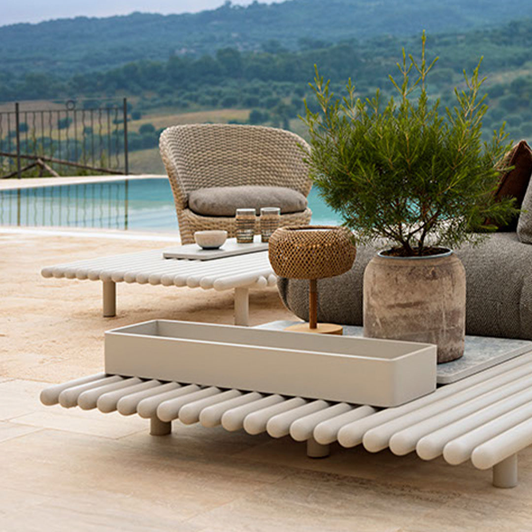 "Terracotta and beige accent furniture with textured patterns, set against a lush green landscape and serene pool."