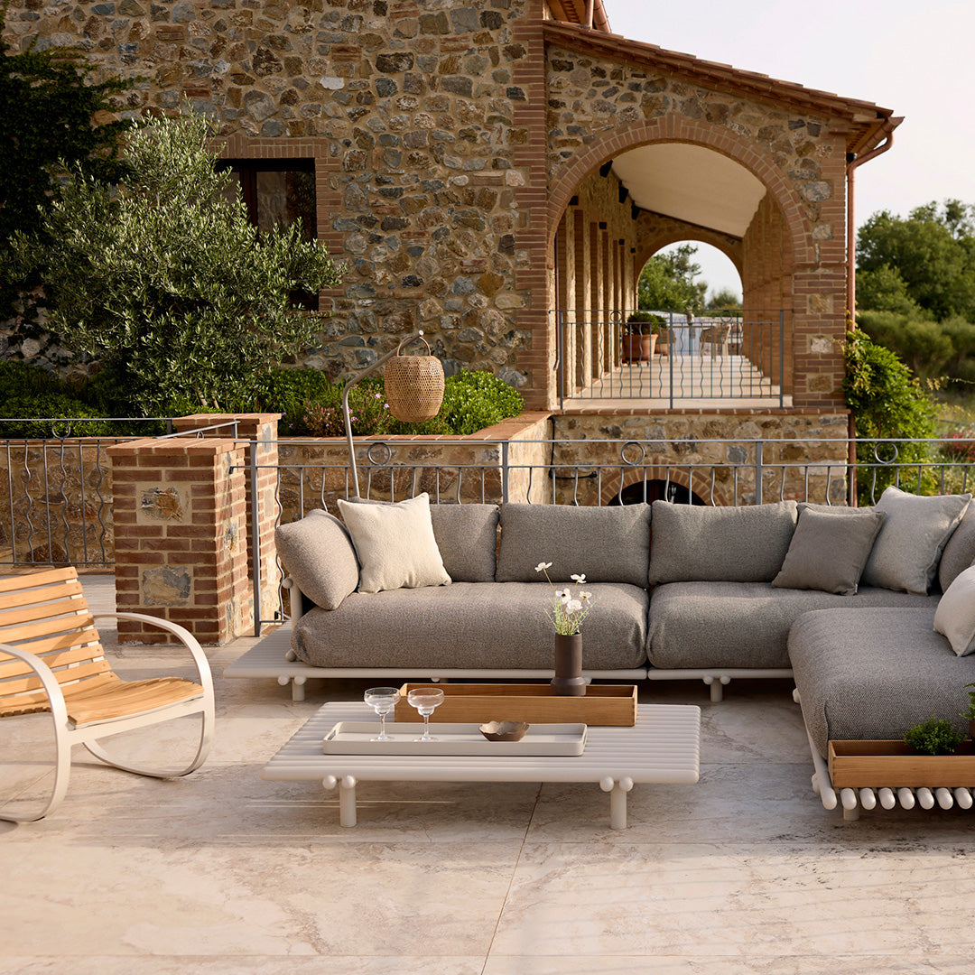 Gray outdoor sectional sofa with soft, neutral cushions, paired with a sleek white coffee table and natural wood accents.