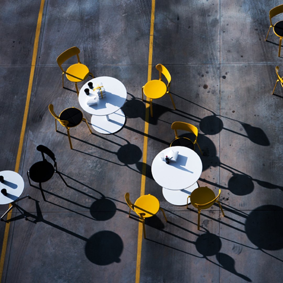 Yellow and black chairs around white tables, casting unique shadows on a textured gray surface.