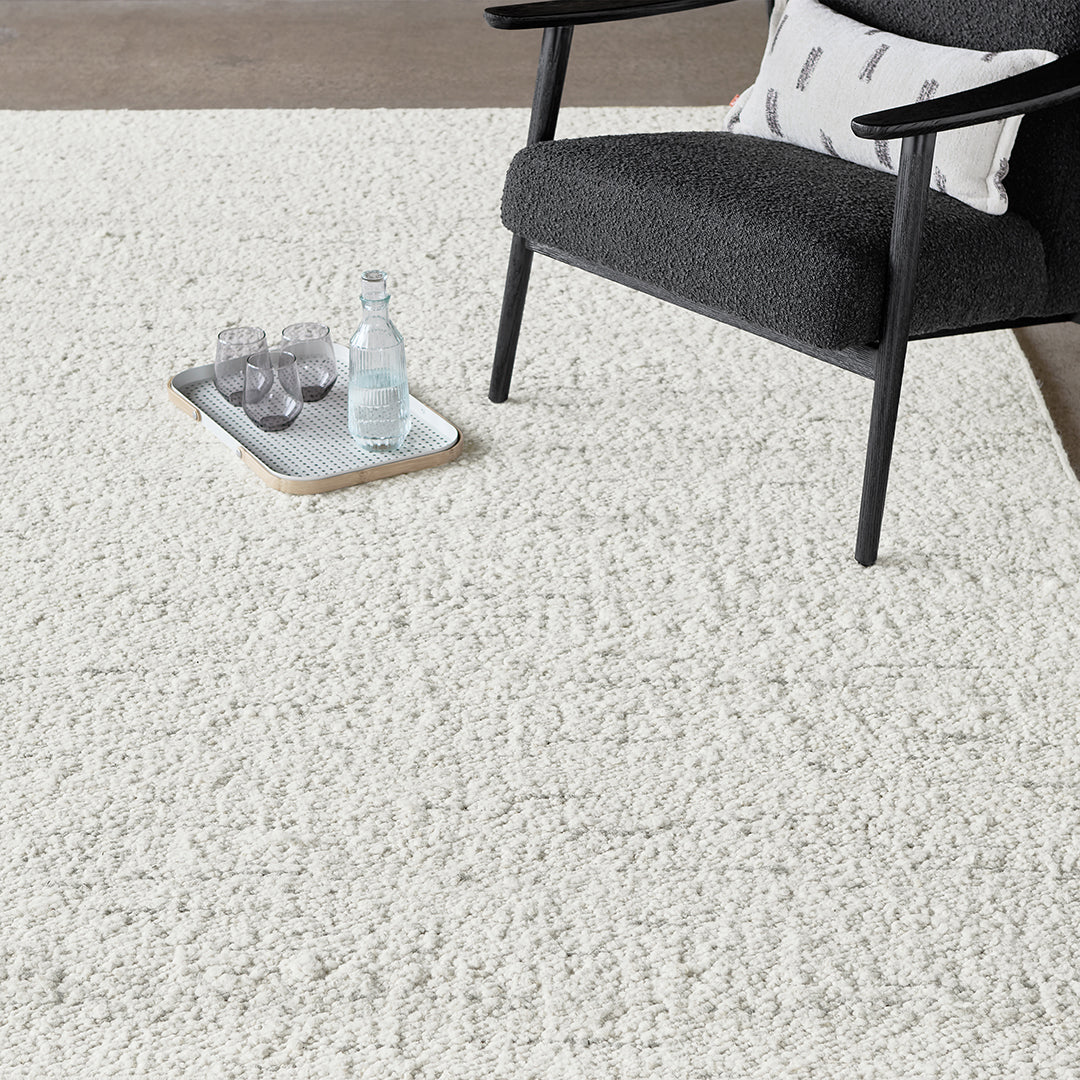 Soft, textured white rug on a light surface, complemented by a dark chair and neutral accessories.