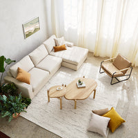 Beige sofa with orange and textured pillows, light wood furniture, and a cream rug in a bright, airy living room.