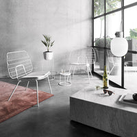 White wire chairs on a gray floor, paired with a pink rug and sleek marble table, set in a modern, minimalistic space.
