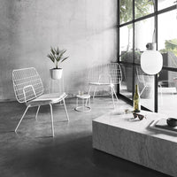 White wire chairs and marble table on a gray concrete floor, featuring minimalistic modern design and a plant accent.