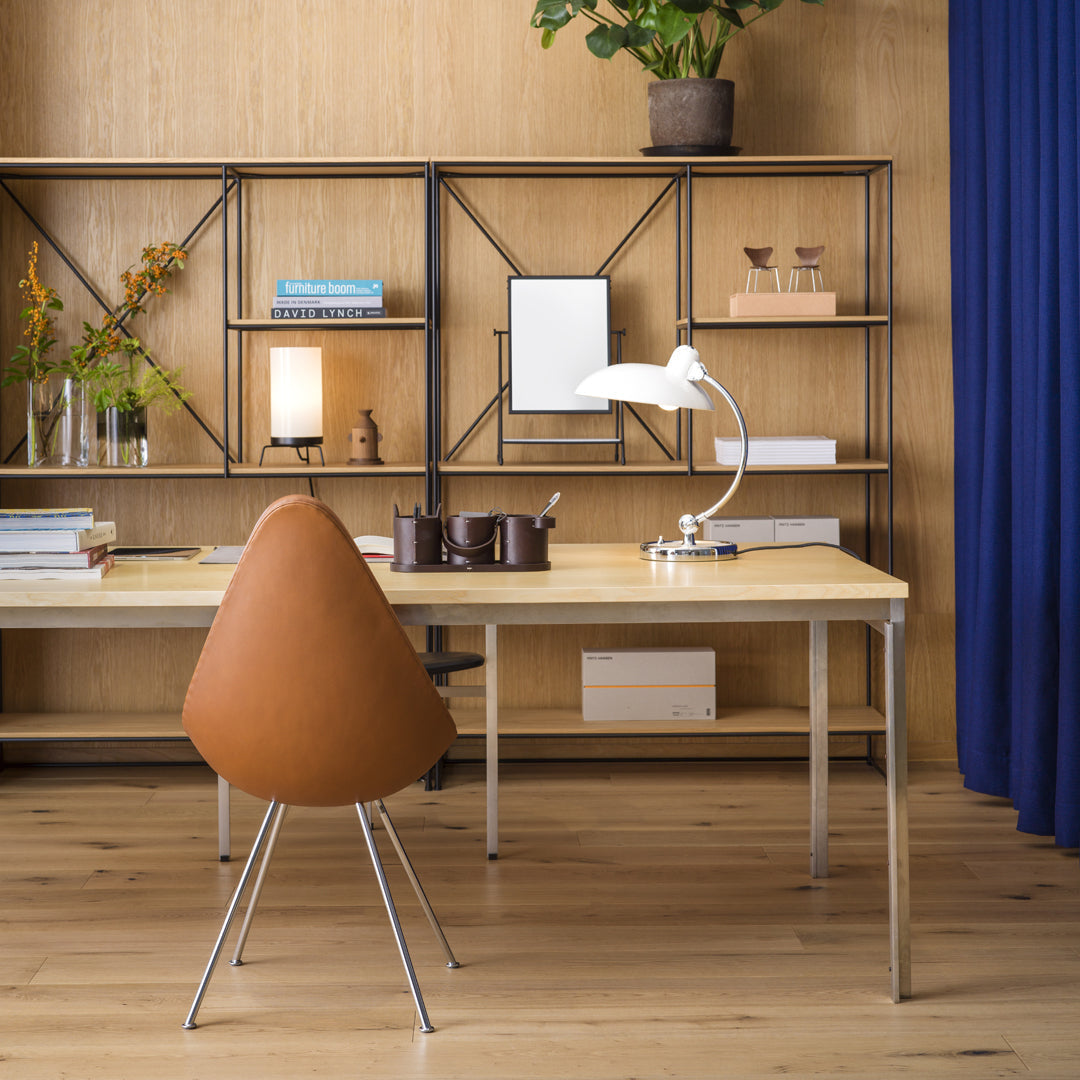 Modern desk with a natural wood finish, brown leather chair, and navy blue curtain, complemented by black metal shelves.