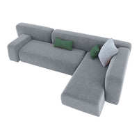 Grey sectional sofa with solid fabric and decorative green and white cushions. Modern and minimalist design.