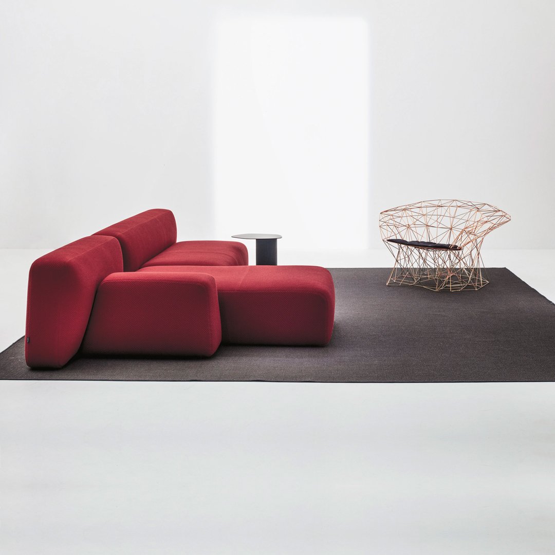 Modern red sectional sofa on a black rug, complemented by a unique woven chair against a minimalist backdrop.