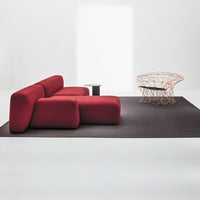 Red modern sofa on a black rug, featuring soft, curved shapes and a minimalist background. 