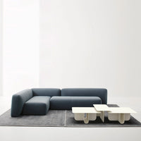 Modern navy blue sectional sofa with a sleek white coffee table on a textured grey rug, creating a minimalist aesthetic.