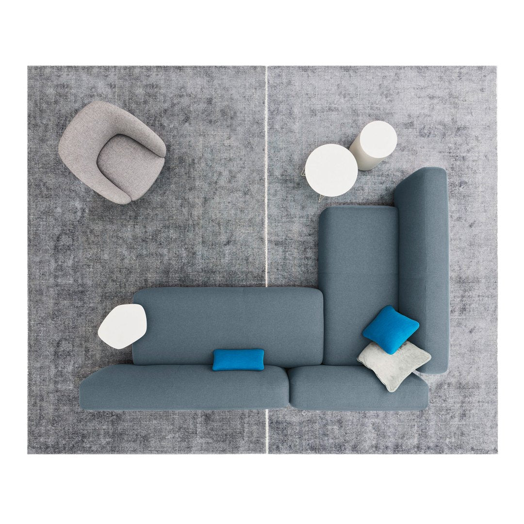 Top view of a grey sectional sofa with blue and white accent pillows on a textured grey rug. Modern and stylish design.