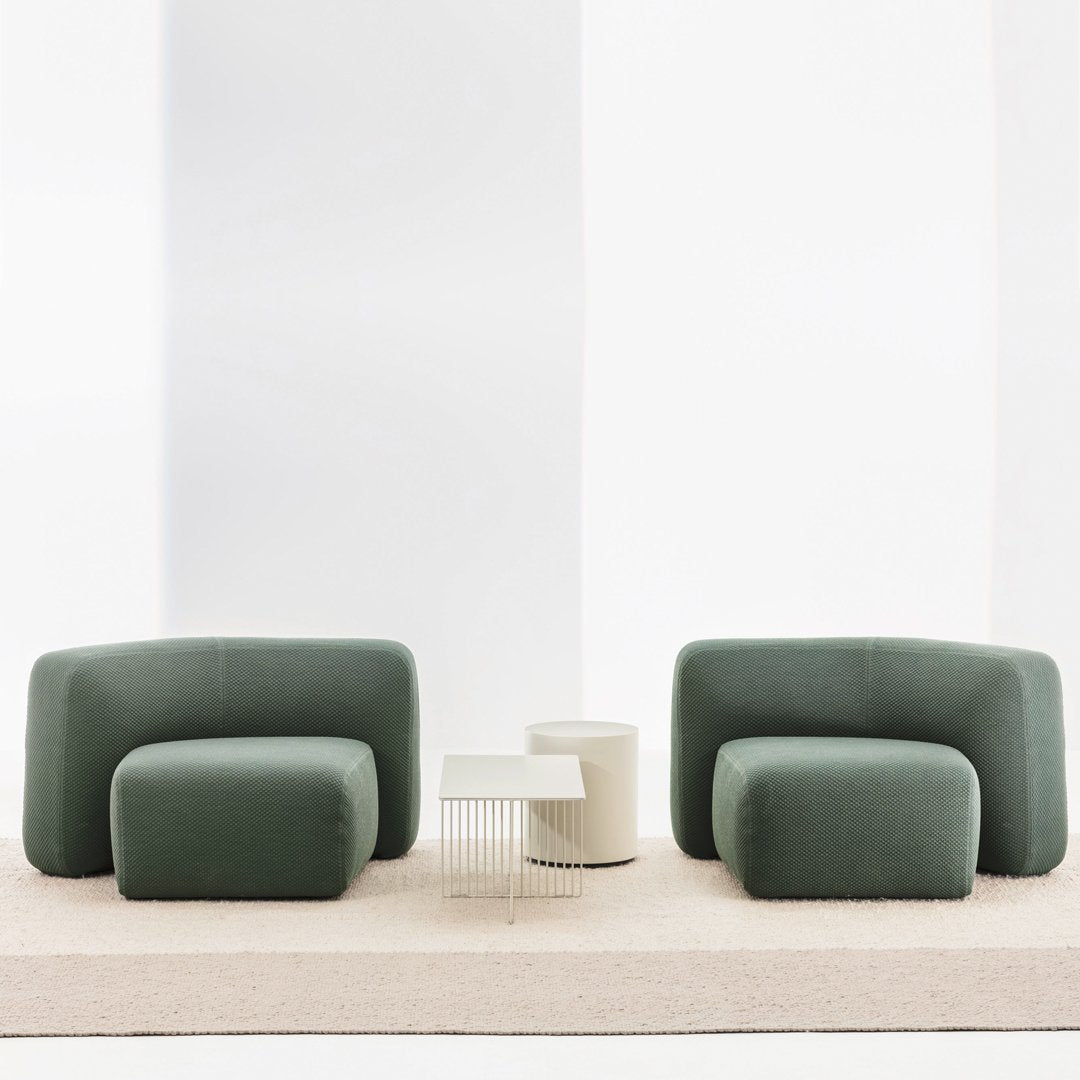 Green curved sofas with a modern design, complemented by a minimalist white side table on a neutral rug.