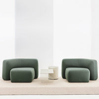 Green curved sofas with a modern design, complemented by a minimalist white side table on a neutral rug.