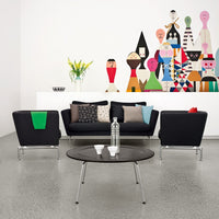 "Modern living room with black furniture, colorful patterned cushions, and a vibrant wall mural featuring abstract figures."