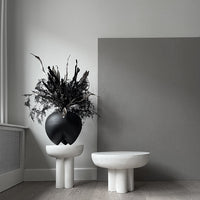 Black vase with textured finish, paired with a smooth white bowl, against a muted grey backdrop. Modern minimalism decor.