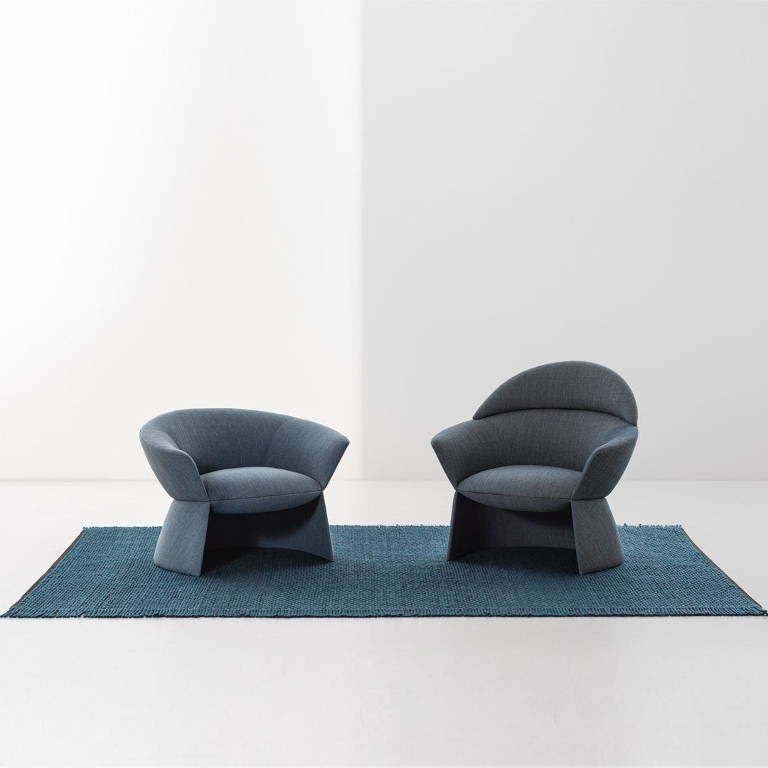 "Two modern chairs in deep blue fabric on a textured teal rug, featuring smooth, curved shapes."
