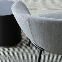 Gray upholstered accent chair with curved design beside a black cylindrical side table on a patterned floor.