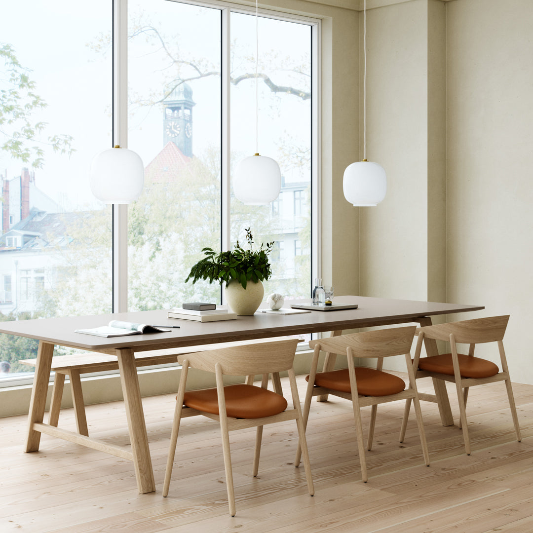 Modern dining table with light wood finish and tan-orange cushioned chairs set against a neutral wall and natural light.