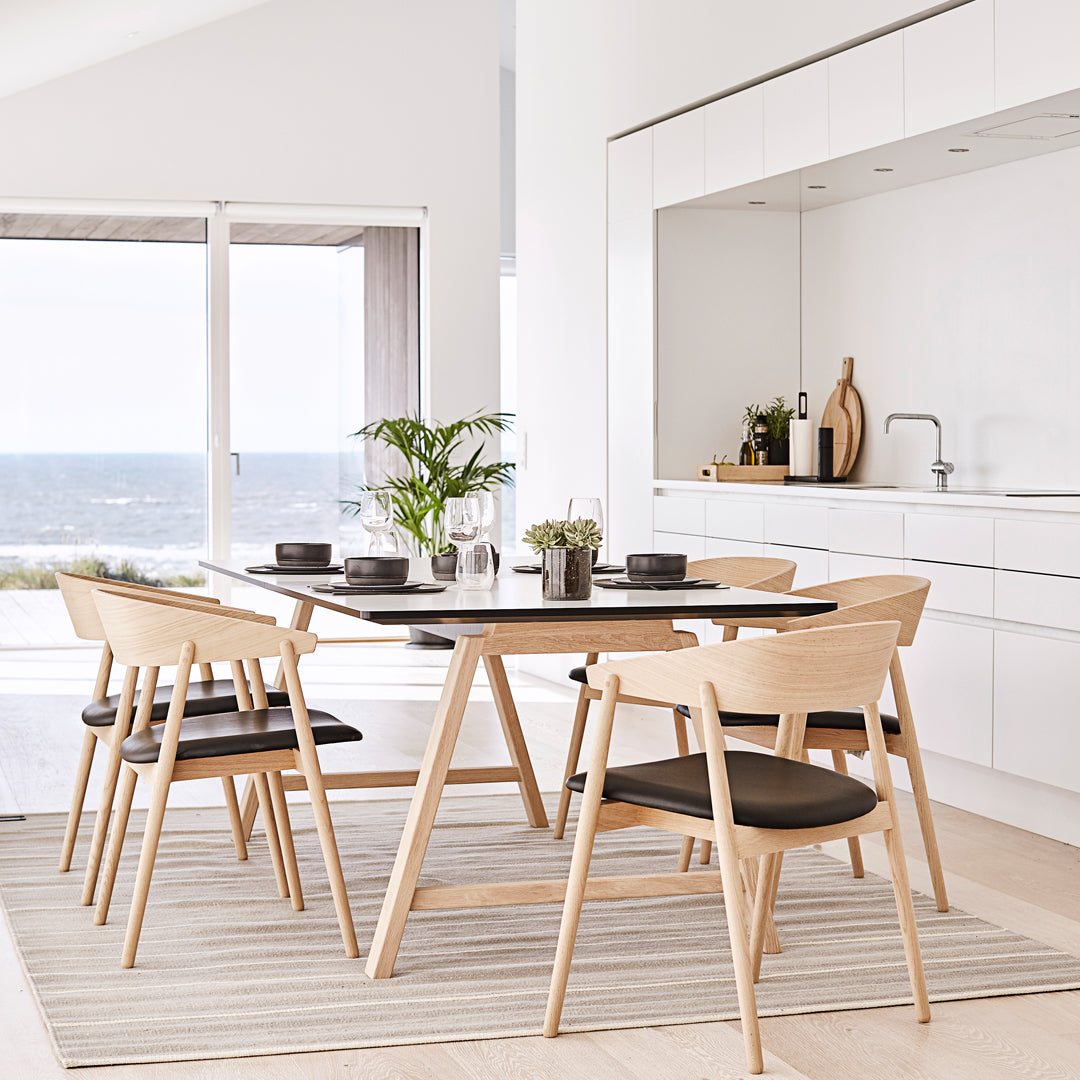 Scandinavian dining set with black table, light wood chairs, and neutral striped rug; modern coastal decor.