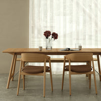 "Minimalist dining room with light wooden furniture, earthy brown chair cushions, and soft, sheer white curtains."