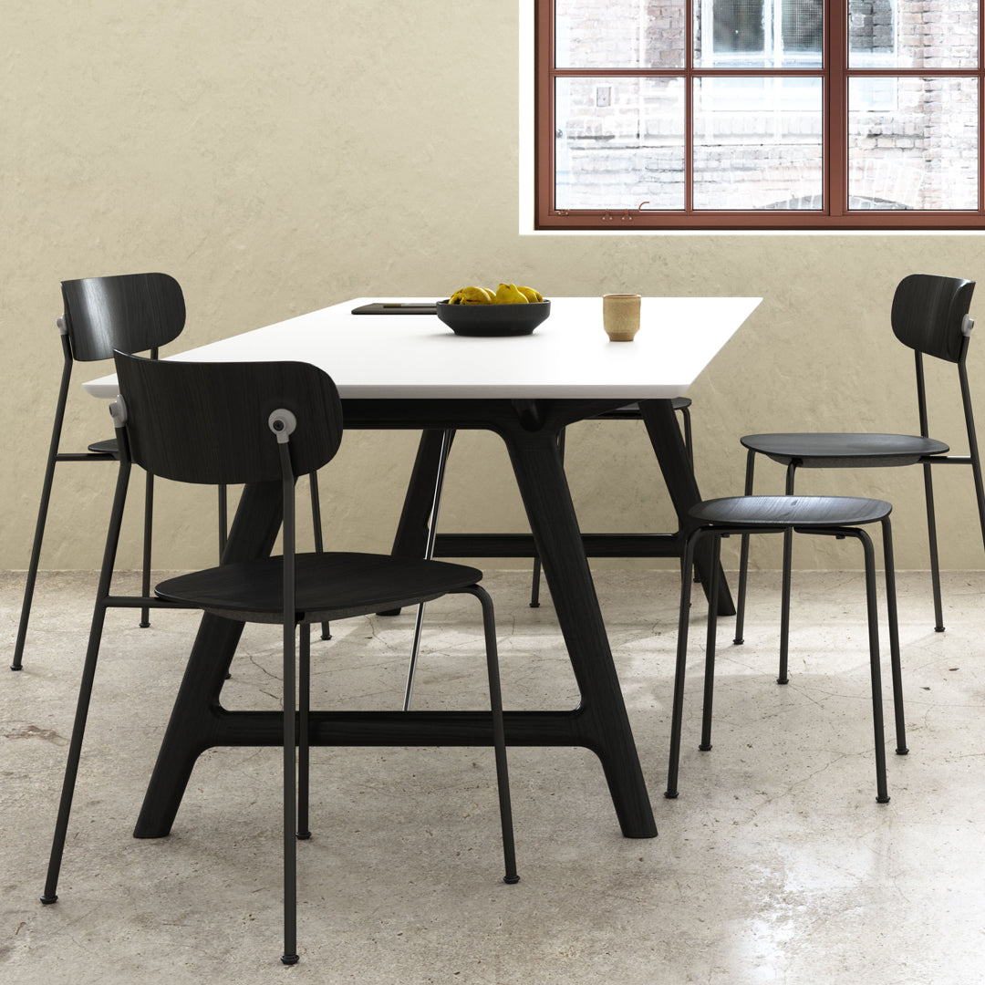 Modern dining table with a white top and black legs, surrounded by black chairs in a minimalist setting.