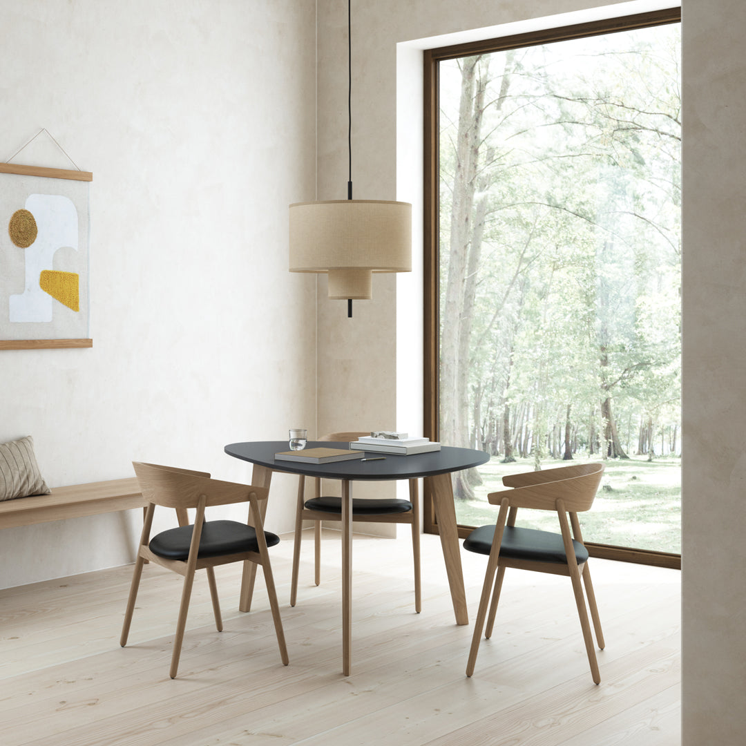 Modern round black table with light wood chairs, soft beige pendant light, and neutral wall tones.