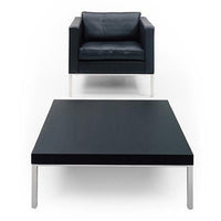 Modern black armchair with plush cushions and sleek flat black coffee table, both featuring minimalistic silver legs.