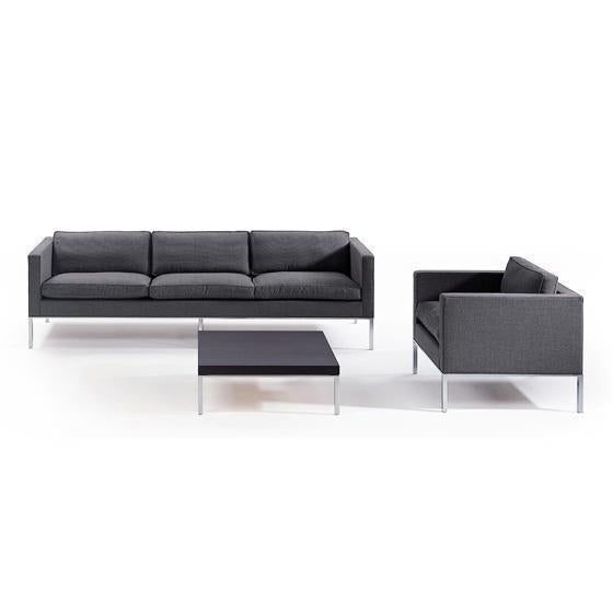 Modern gray sofa and armchair set with sleek chrome legs and a minimalist black coffee table.