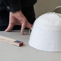 White hat with a smooth surface, featuring a subtle pattern, alongside a measuring tool on a neutral tabletop.