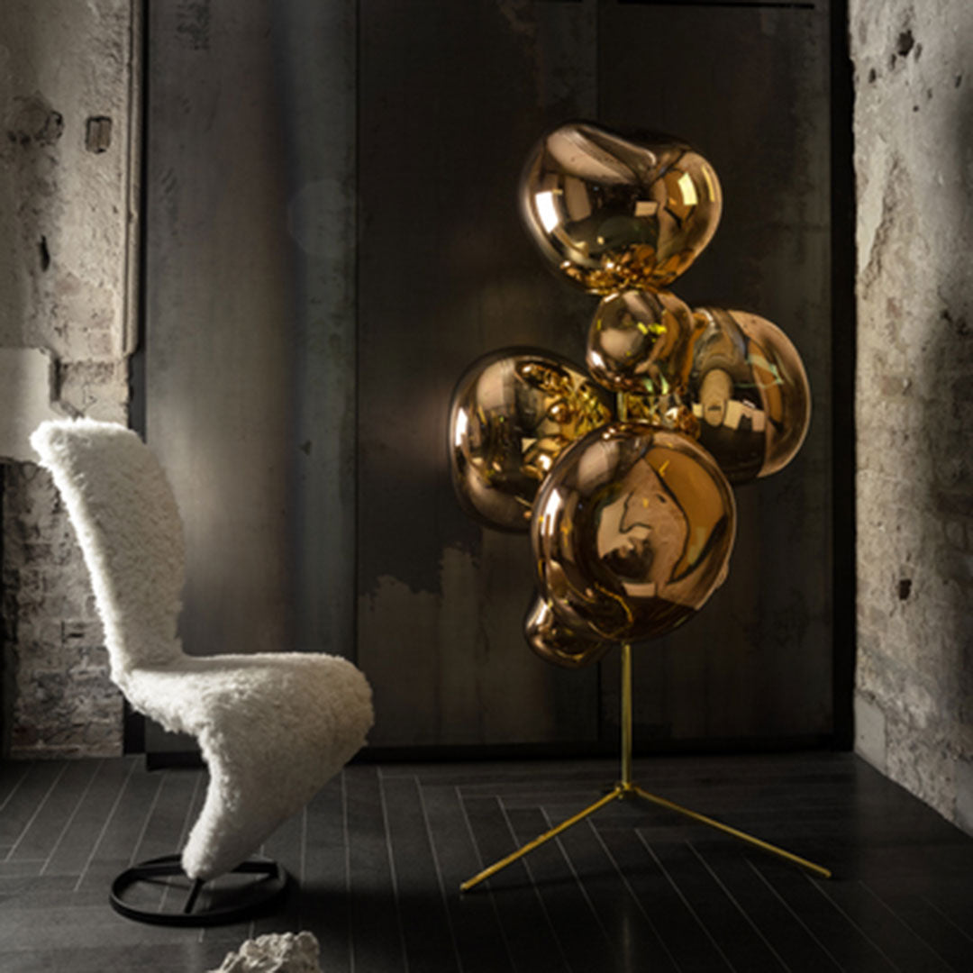 "Shiny gold balloon decor with a modern gold stand, complementing a textured white chair against an industrial background."