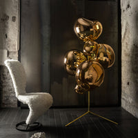 "Shiny gold balloon decor with a modern gold stand, complementing a textured white chair against an industrial background."
