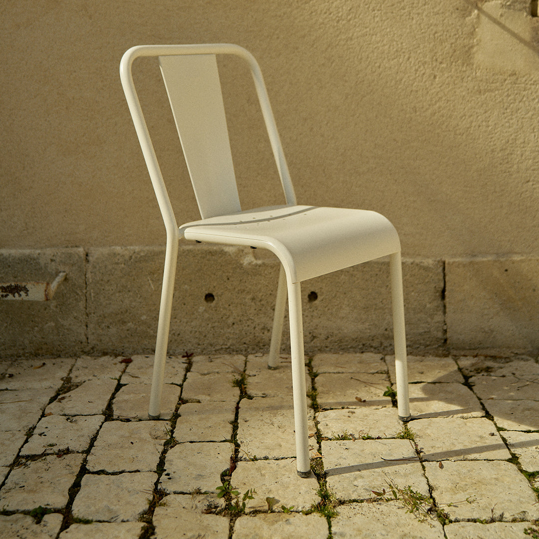 White metal chair with a minimalist design, featuring smooth lines and a modern finish against a rustic stone backdrop.