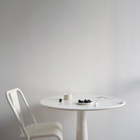 Minimalist white round table with a textured surface, paired with a white chair against a soft gray wall.