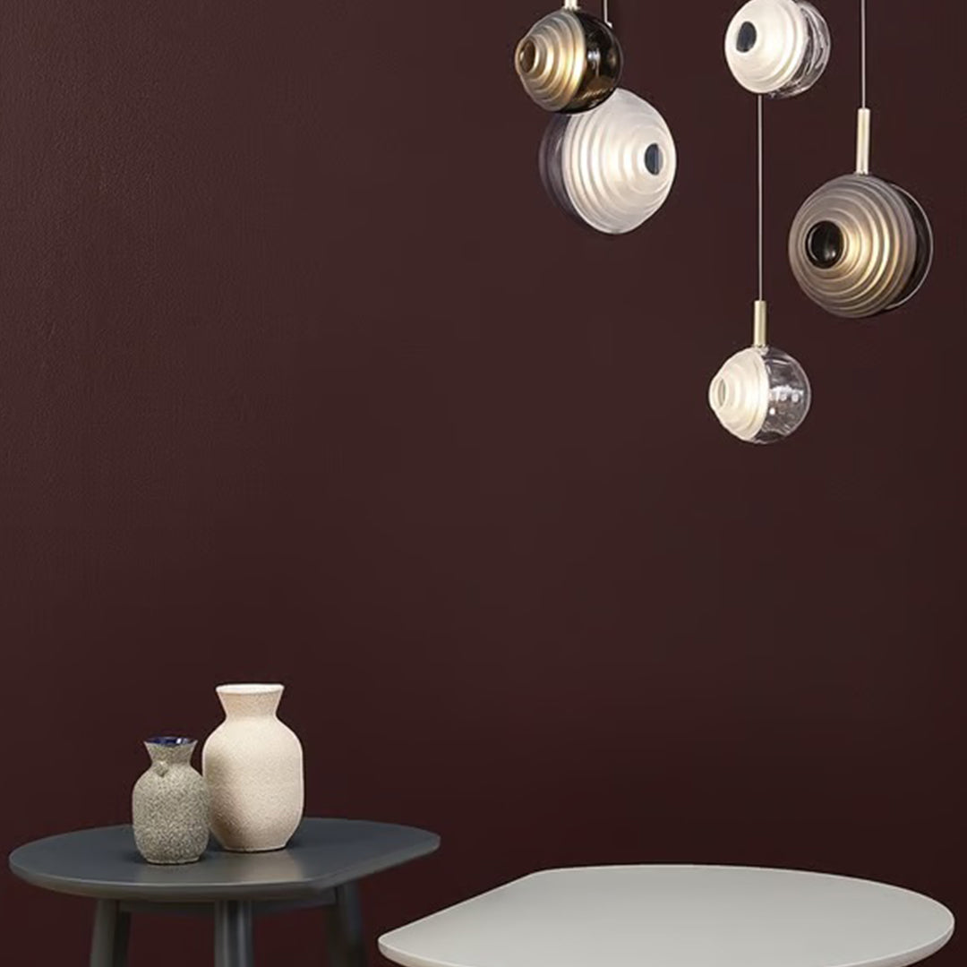 "Modern pendant lamps in gold and white against a rich burgundy wall, featuring sleek circular patterns."