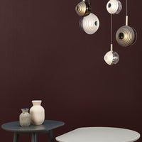 "Modern pendant lamps in gold and white against a rich burgundy wall, featuring sleek circular patterns."