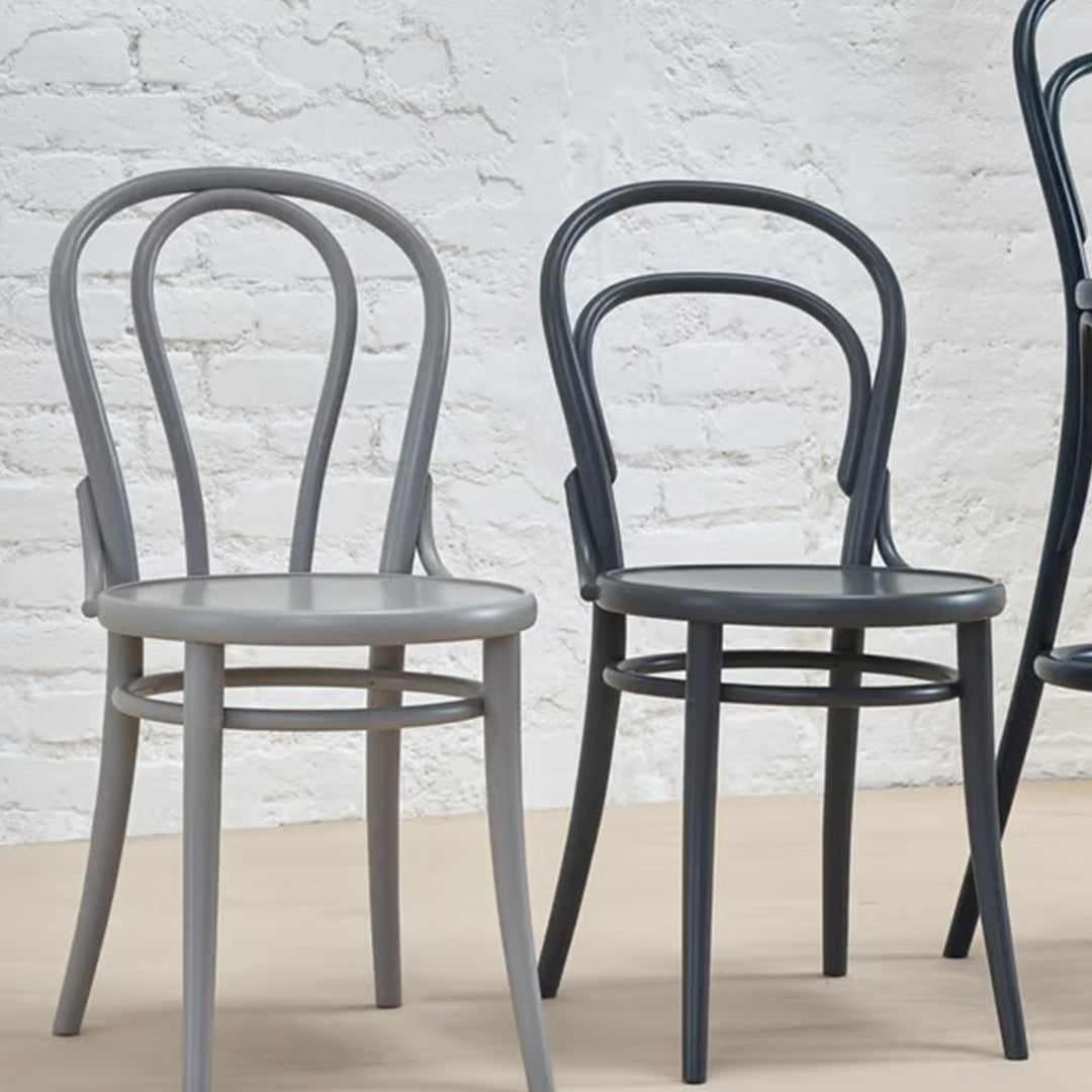 Pair of curved-back chairs in light gray and dark gray against a white brick wall, showcasing sleek, modern designs.